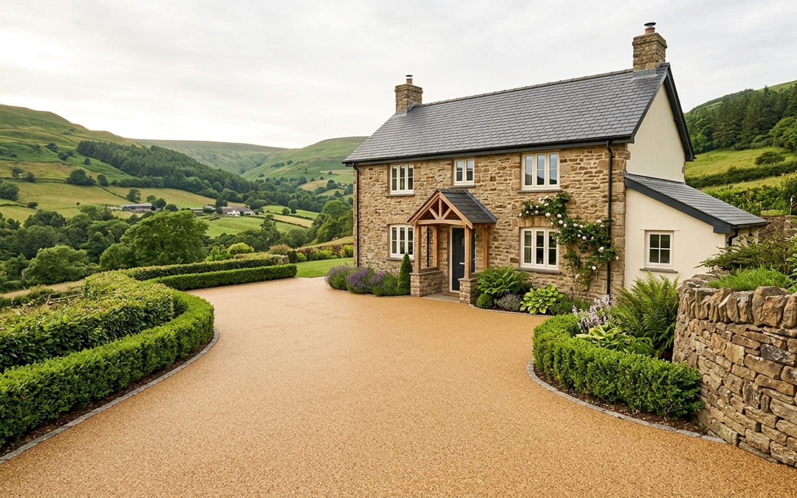 A freshly laid resin-bound driveway in warm honey-gold aggregate leading to a South Wales stone cottage bordered by evergreen hedging